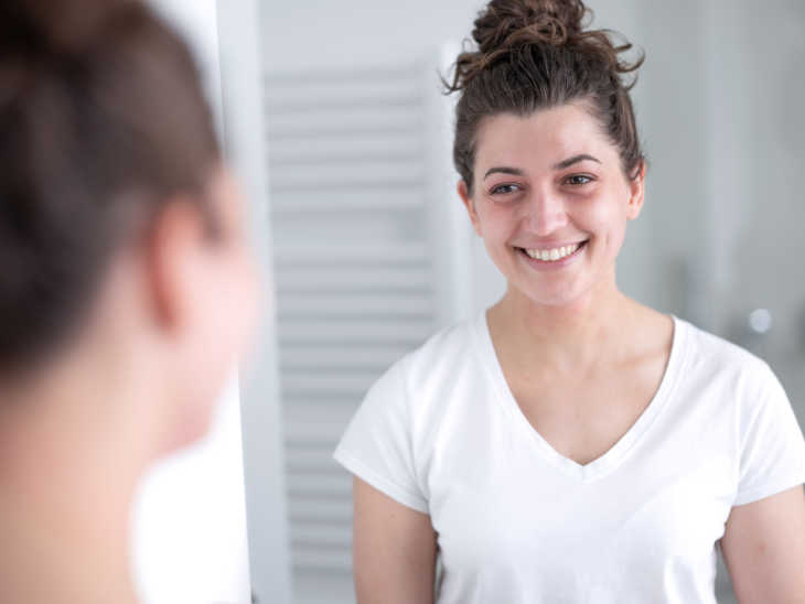 Frau mit Neurodermitis lächelt sich im Spiegel an