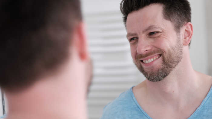 Mann mit Neurodermitis lächelt vor dem Spiegel