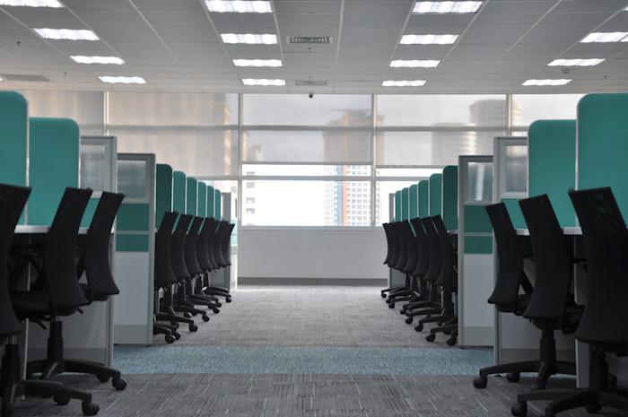 An empty office with a dozen office chairs lined in cubicles.
