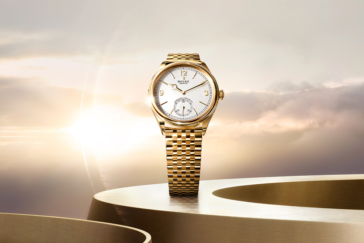 A luxurious wristwatch featuring a light blue face with silver accents and a small sub-dial. The watch has a polished silver case and a brown leather strap, shown unbuckled. The background is a smooth gradient of pale blue and white.