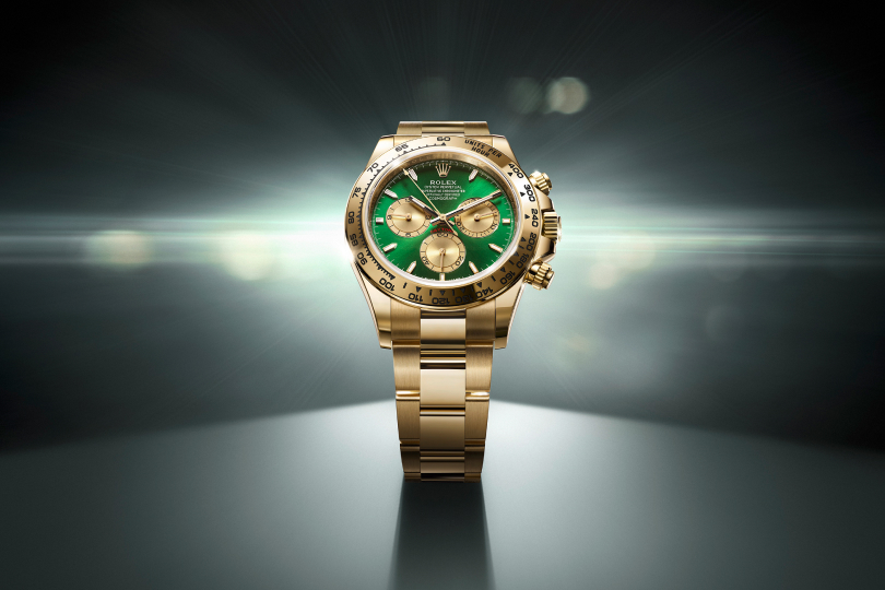 A polished, silver luxury wristwatch with a black dial and three sub-dials is displayed against a dark, gradient background with a subtle light flare, emphasizing its sleek, metallic design and intricate details.