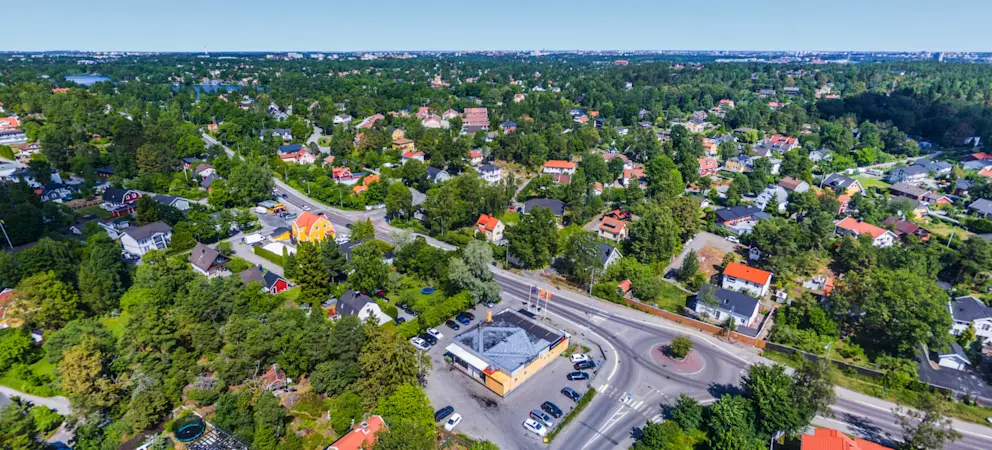 Flygvy över Huddinge med villaområde, grönska, vägar och bostäder i ett lugnt och naturnära område nära Stockholm.