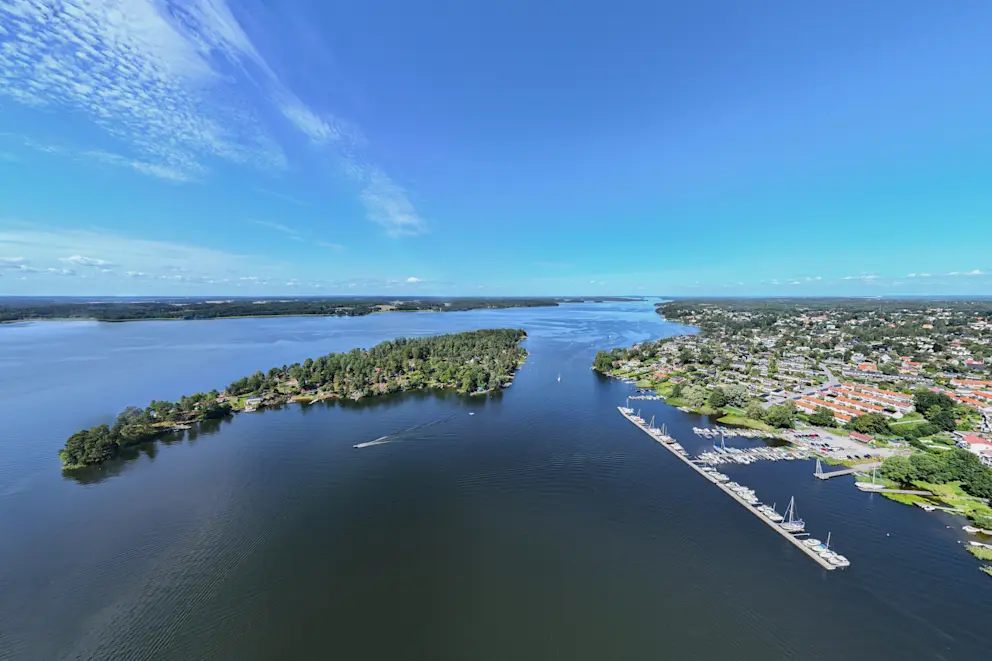 Flygvy över Hässelby-Vällingby med Mälaren, småbåtshamn, grönska och bostadsområden i västra Stockholm.