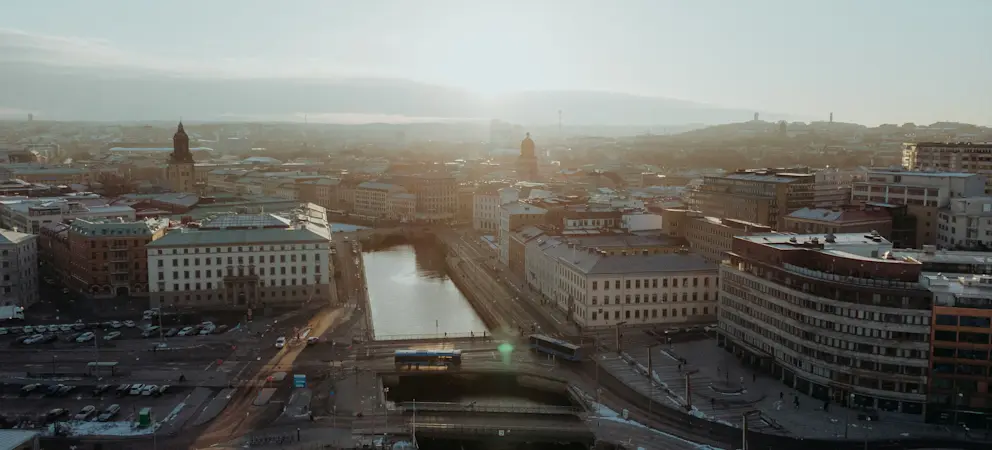 Flygvy över centrala Göteborg med kanal, bro, stadsbebyggelse och morgonljus över stadens takåsar.