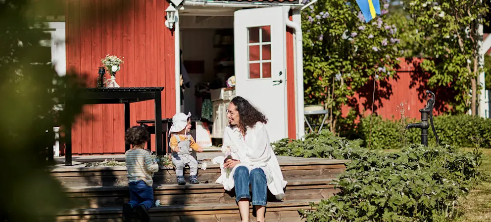 Röd villa med trappa och trädgård där flera personer vistas utanför huset, med svensk flagga vid entrén.