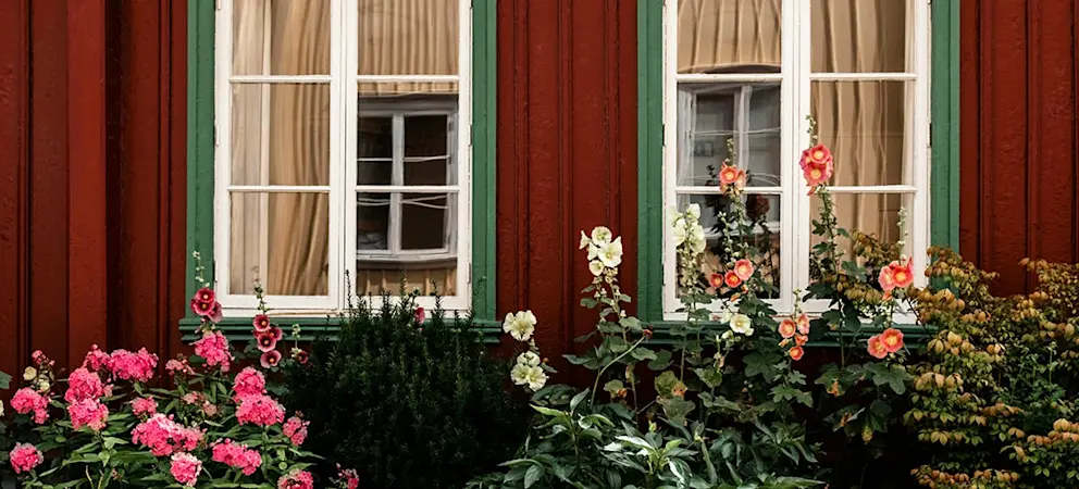 Röd träfasad med spröjsade fönster och blommande trädgård utanför ett traditionellt svenskt hus.