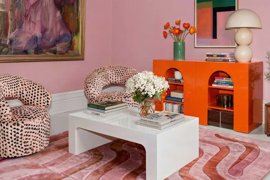 Stilfullt vardagsrum med rosa väggar, färgstark konst, mönstrade fåtöljer och modern inredning.
