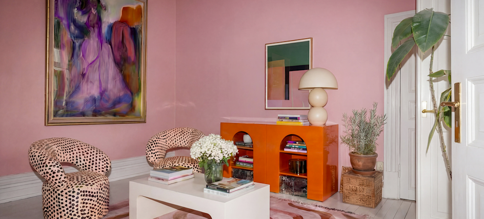 Stilfullt vardagsrum med rosa väggar, färgstark konst, mönstrade fåtöljer och modern inredning.