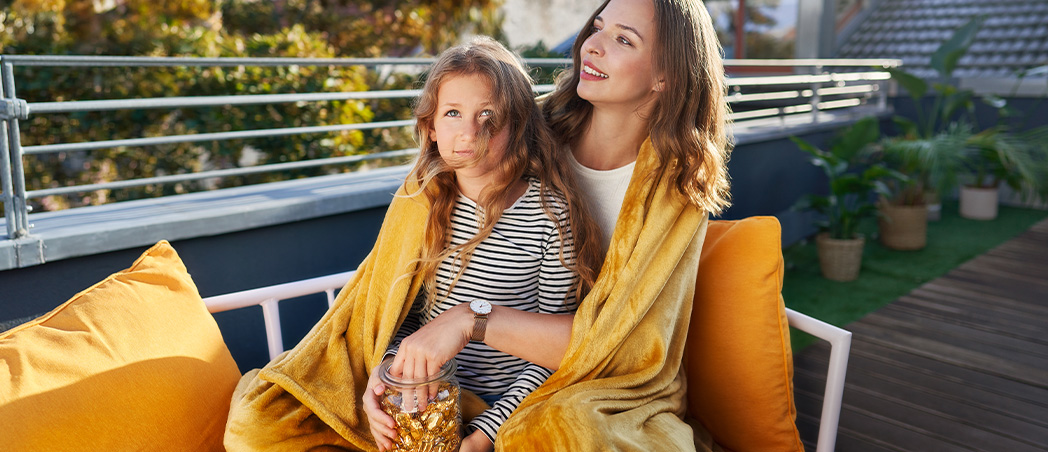 Mutter und Tochter sitzen in eine Decke gehüllt auf einer Bank