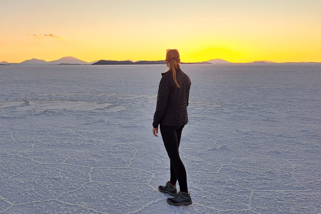Weibliche Person steht in Salzwüste und schaut auf Sonnenuntergang