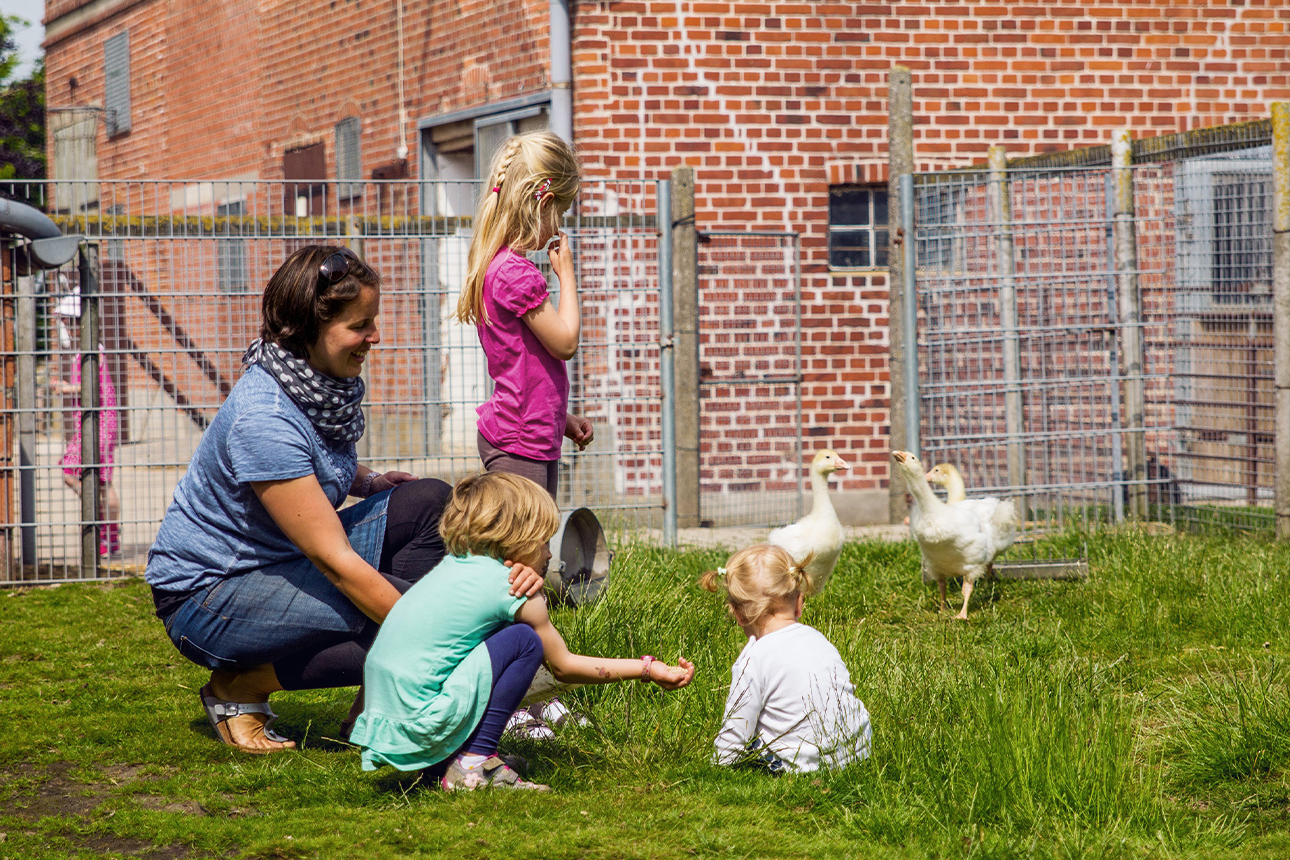 Frau mit Kindern vor einem Hühnerstall