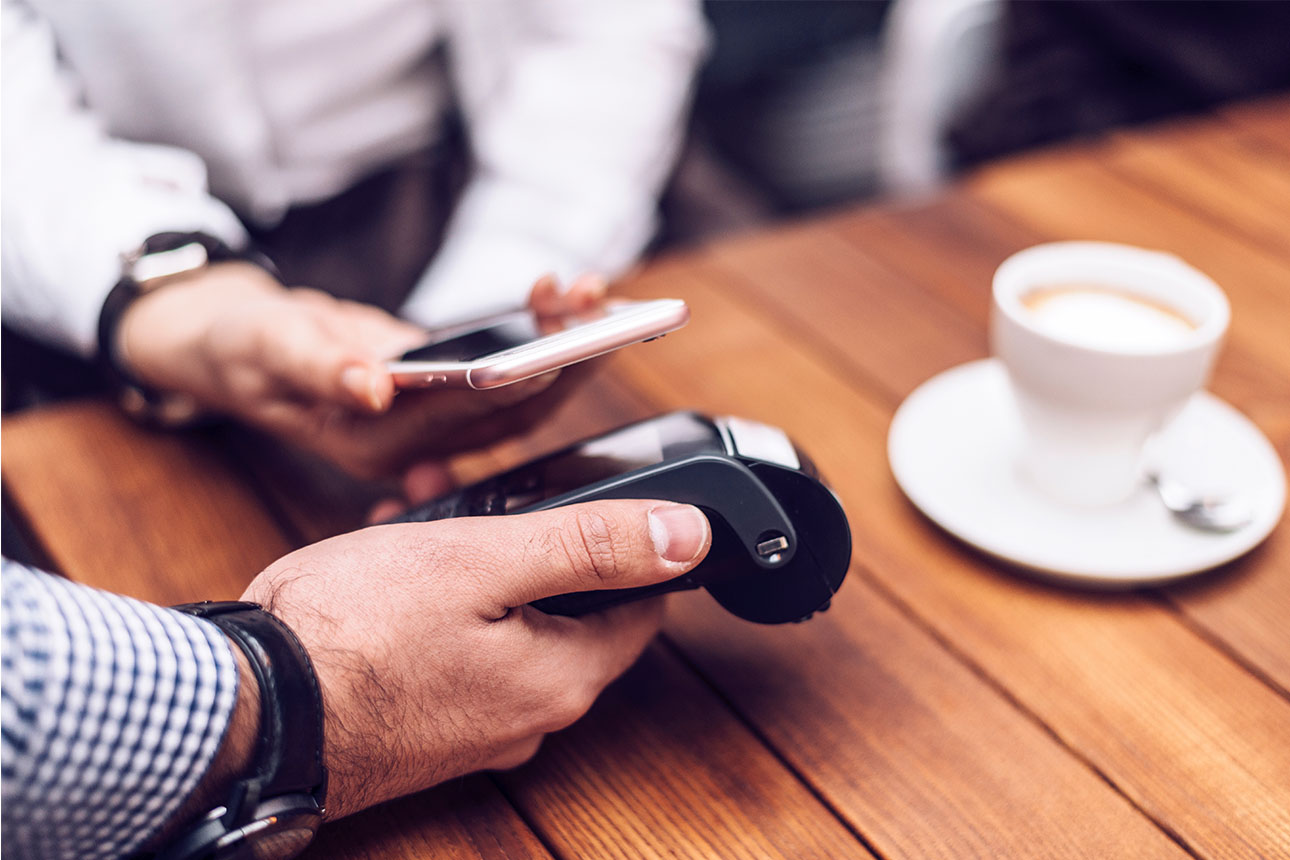 Ein Smartphone bei einer kontaktlosen Zahlung an einem Bezahlterminal im Cafe