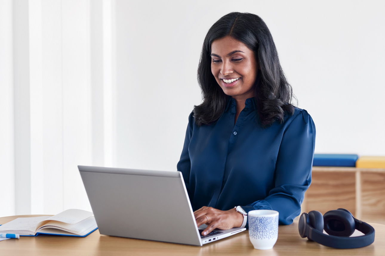 DKB-Trainee Sangavi lächelnd beim Arbeiten am Laptop