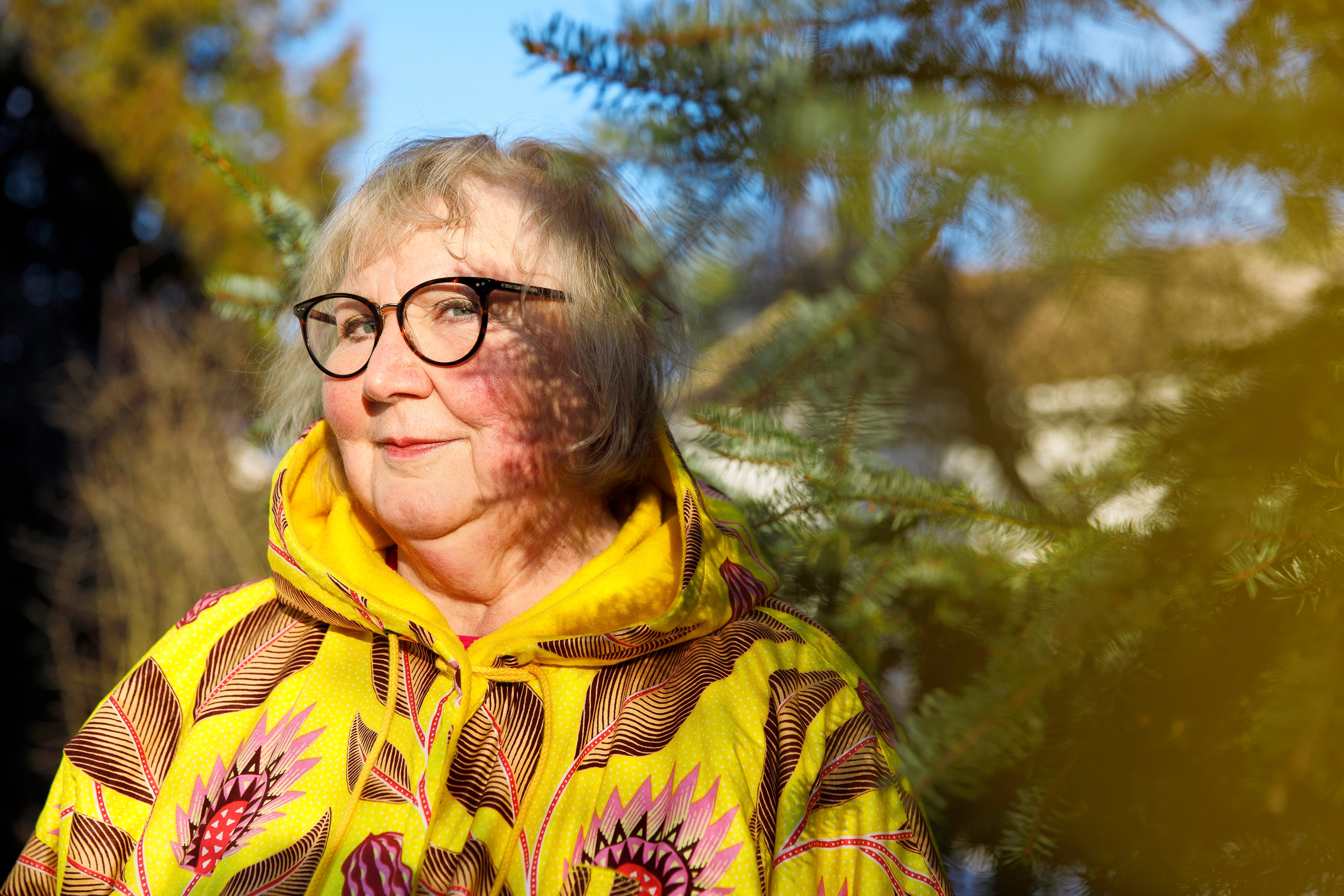 Anneli Kanto hymyilee ja katsoo kameraan puun oksan katveessa