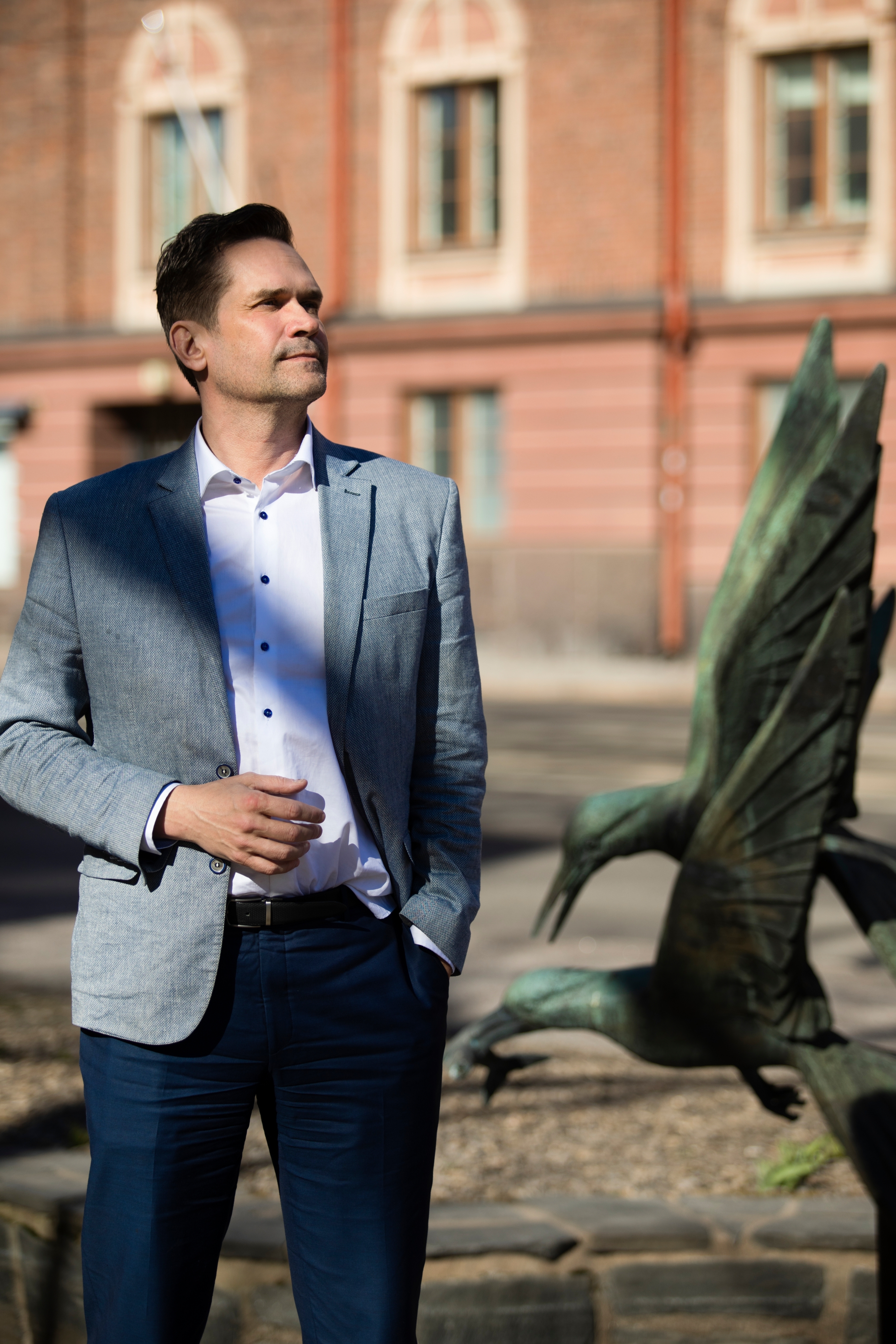 Mika Aaltola seisoo ulkona kadulla lintupatsaan edessä