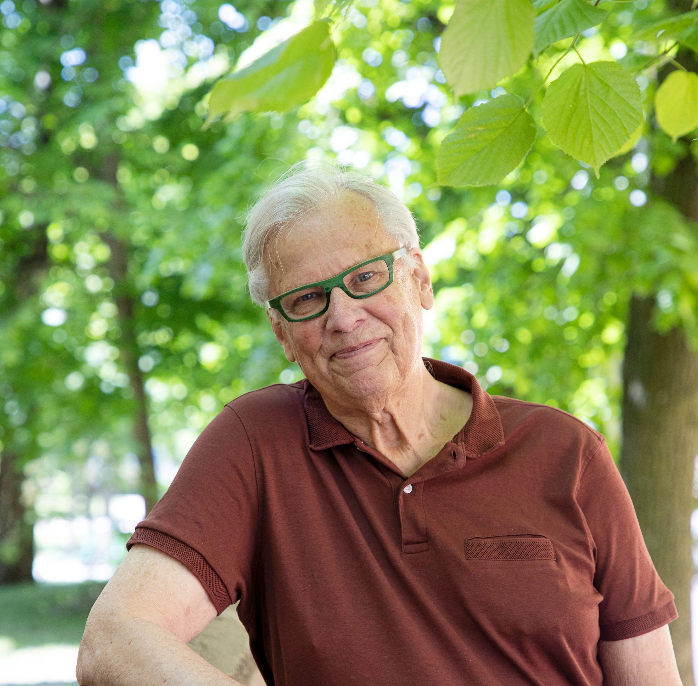 Wenzel Hagelstam nojaa ulkona aitaan ja katsoo kohti hymyillen.