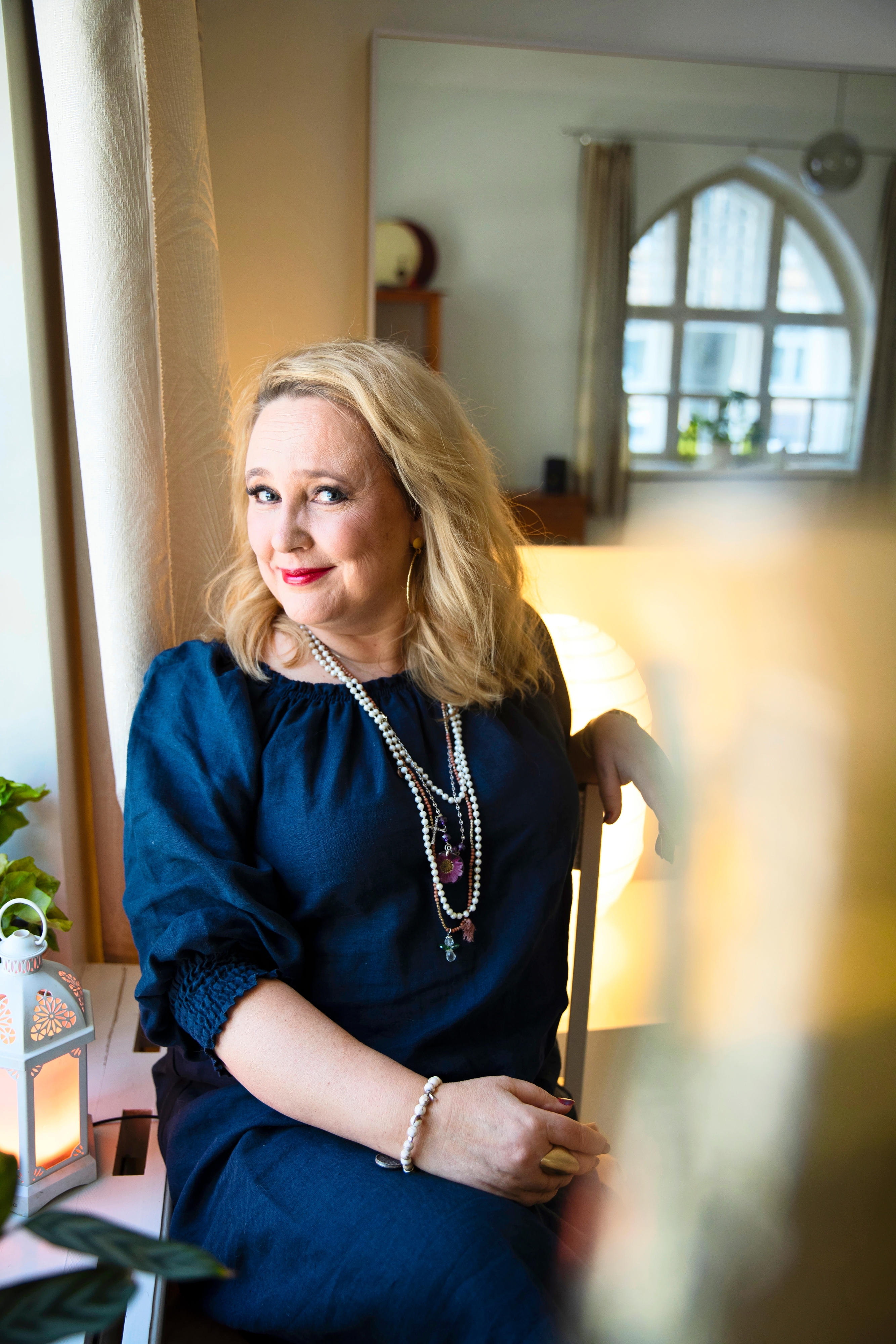 Eeva Pesonen istuu tuolilla ja katsoo hymyillen kameraan
