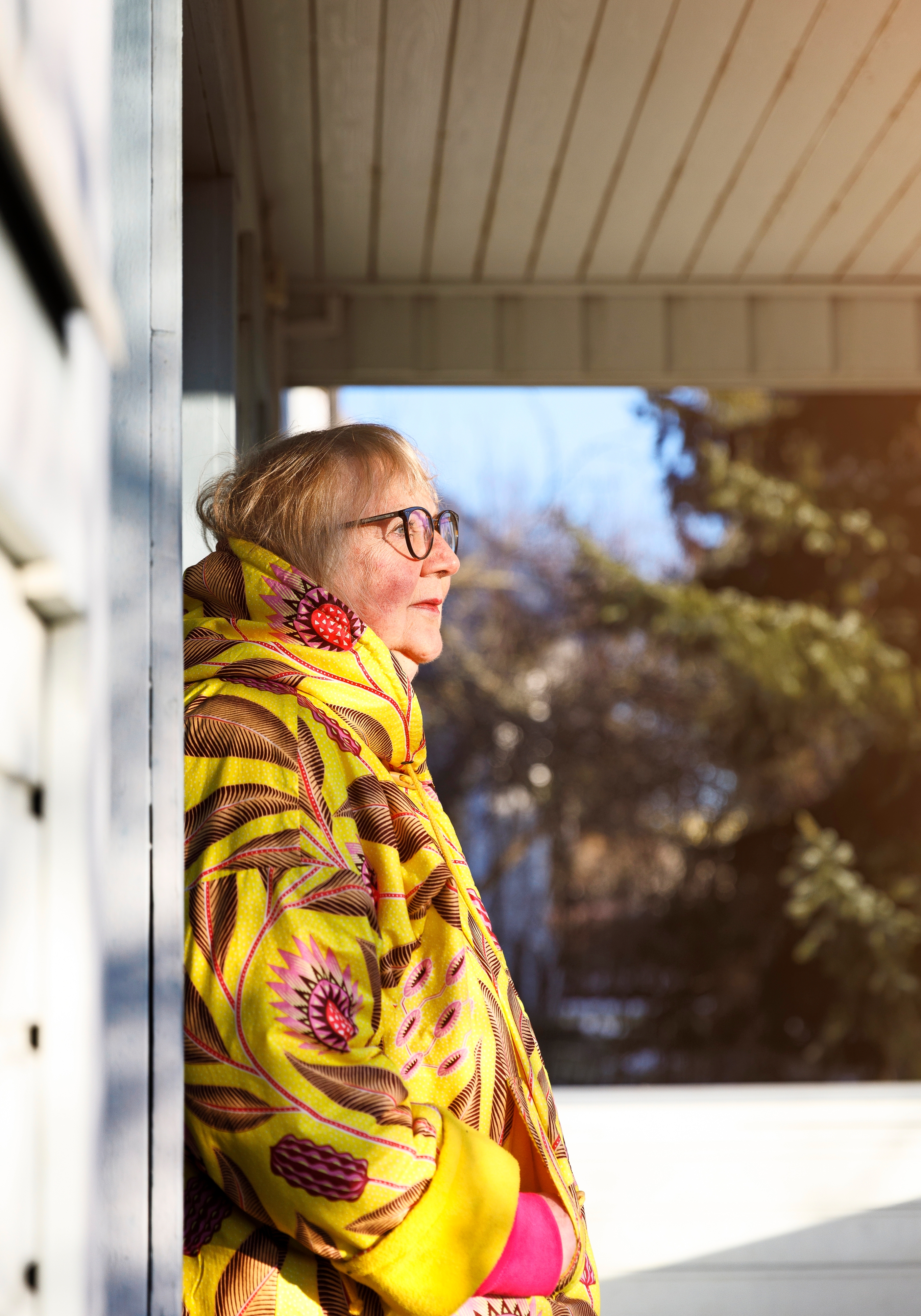 Anneli Kanto nojaa talon ulkoseinään ja katsoo oikealle