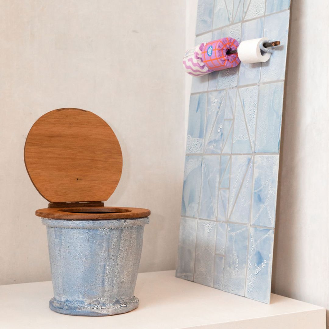 A blue toilet with wooden seat on a plinth next to a blue tiled wall and toilet roll holder