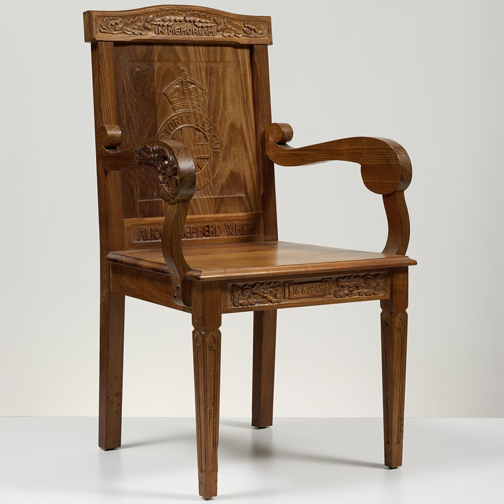 A carved wooden chair with scrollwork on the arms and legs tapering down to a point