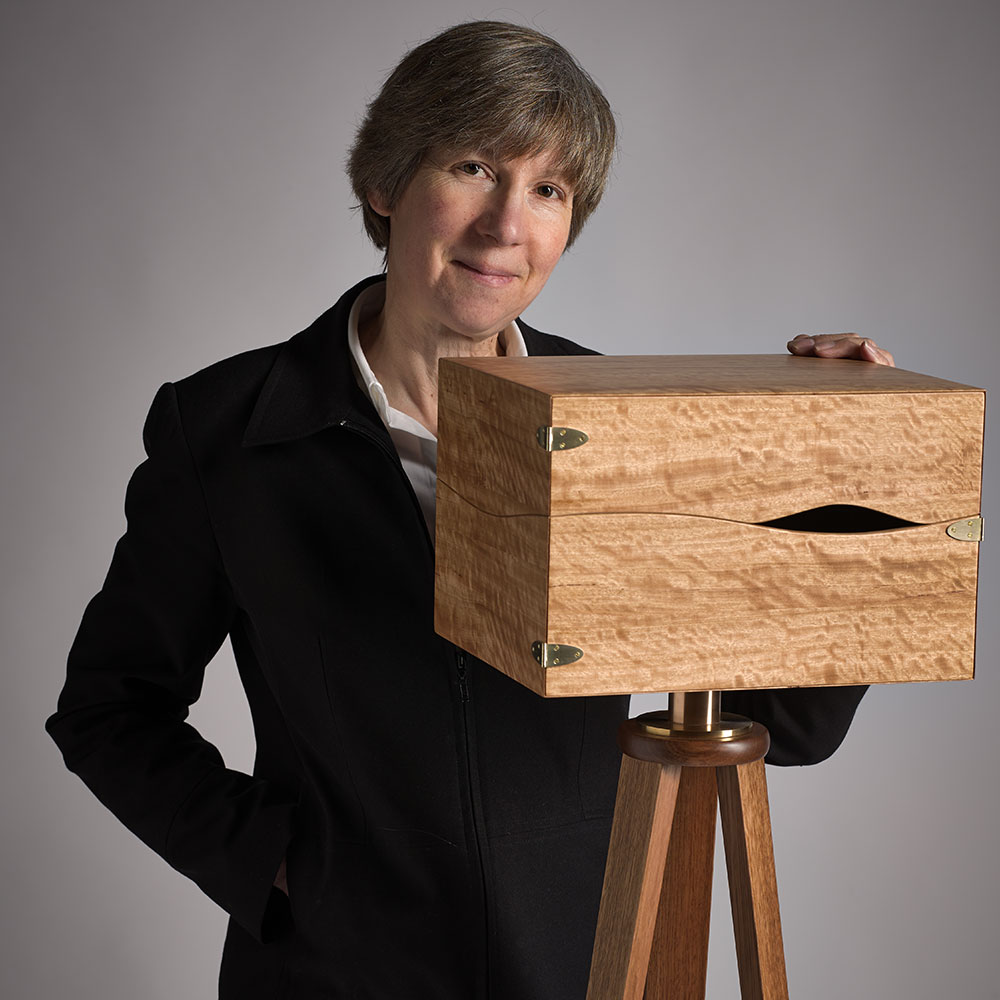 An image of Linda standing next to a wooden box on a tripod