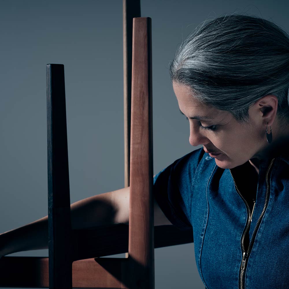 A woman wearing a blue denim shirt looks down at a series of interlocked wooden pieces