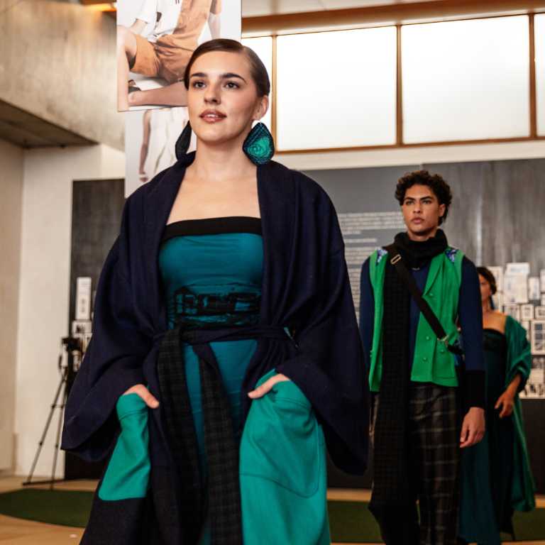 A model wearing a deep teal gown with dark wrap