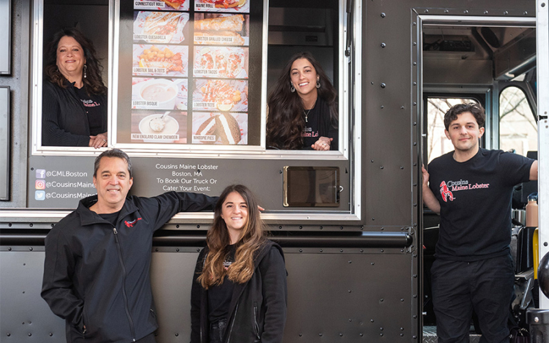 A family photo of our Cousins Maine Lobster Boston Franchise owners standing around their food truck proudly.