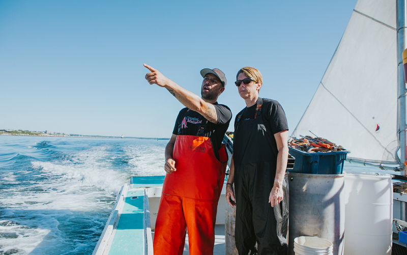 A photo of our Columbus franchisee standing with Cousin Sabin on a lobster boat as he points off to something in the distance.