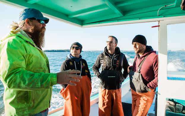 A Maine Lobsterman speaking to some members of Cousins Maine Lobster aboard a lobster boat.