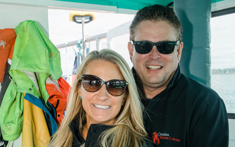 A photo of our two Cousins Maine Lobster franchise owners in sunglasses smiling on a fishing boat in Maine.