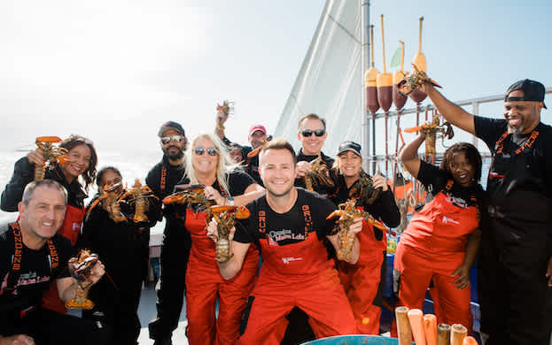 A group of Cousins Maine franchisees, all holding lobsters on a lobster boat, while training and learning about the Maine Lobster industry in Maine.