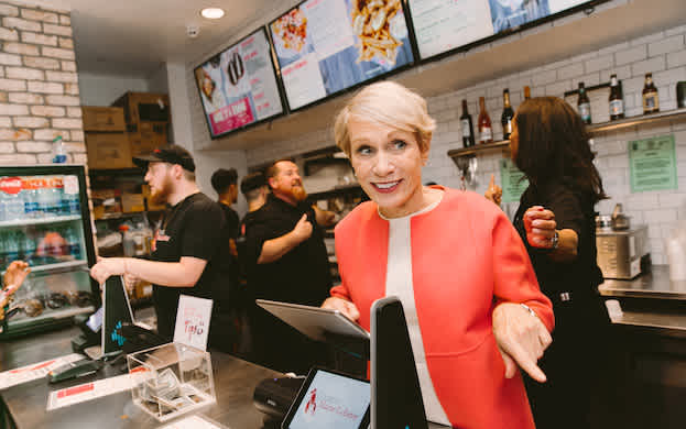 Barbara Corcoran standing behind a register at a Cousins Maine Lobster location, having fun.