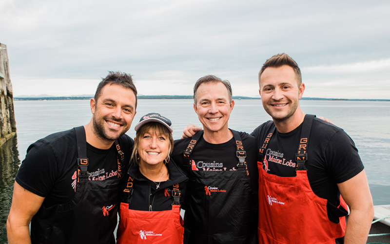 A photo of our Raleigh owners with Cousins Maine Lobster founders, Jim & Sabin, dressed in fishing gear.