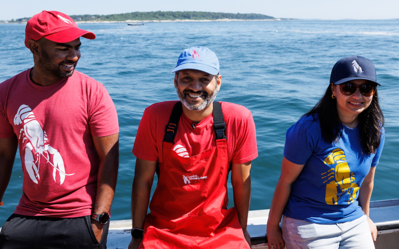 An image of three of our SF Bay and Denver family members sitting on the gunwale of a lobster boat, smiling at the camera