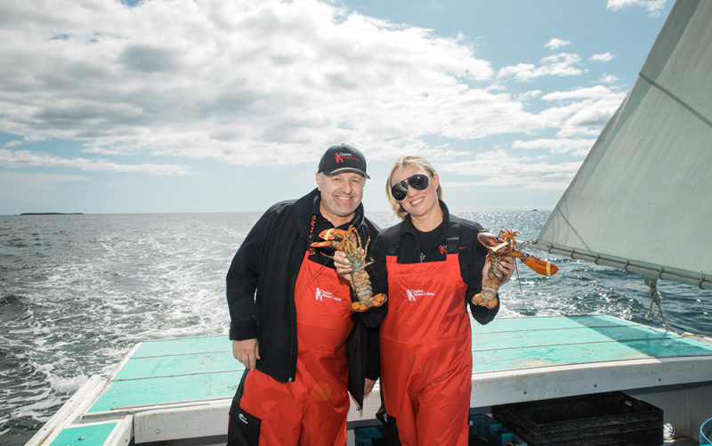 A photo of our Freehold franchisees standing on the back of a lobster boat on a sunny day, holding lobsters.