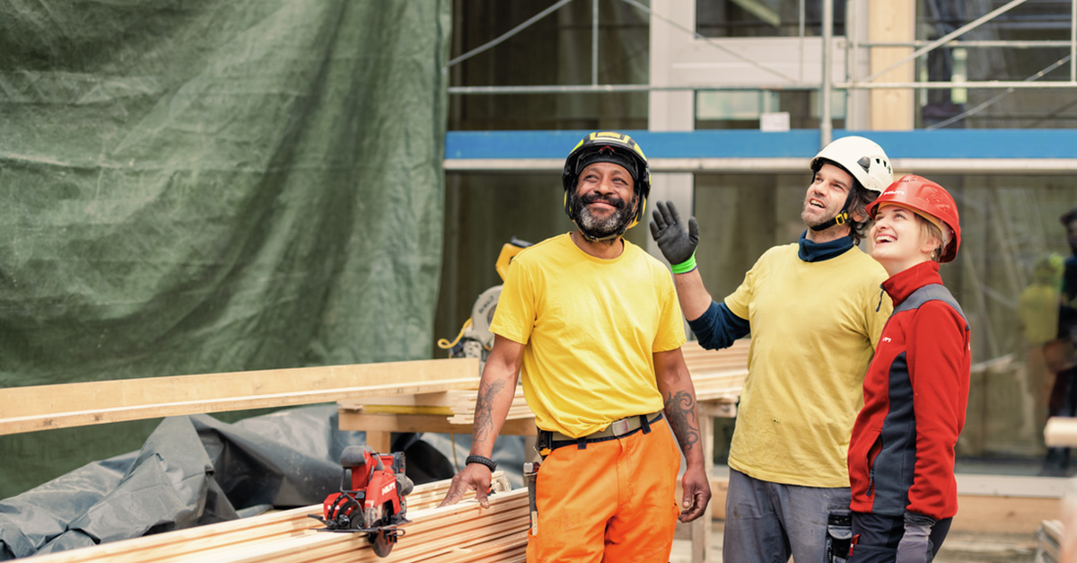 Two construction site workers and a Hilti representative smile on a wood construction site.