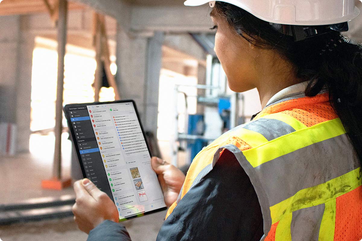 A female construction worker going through her task list on Fieldwire. She is using her iPad in the field to ensure that all the tasks are being completed correctly.