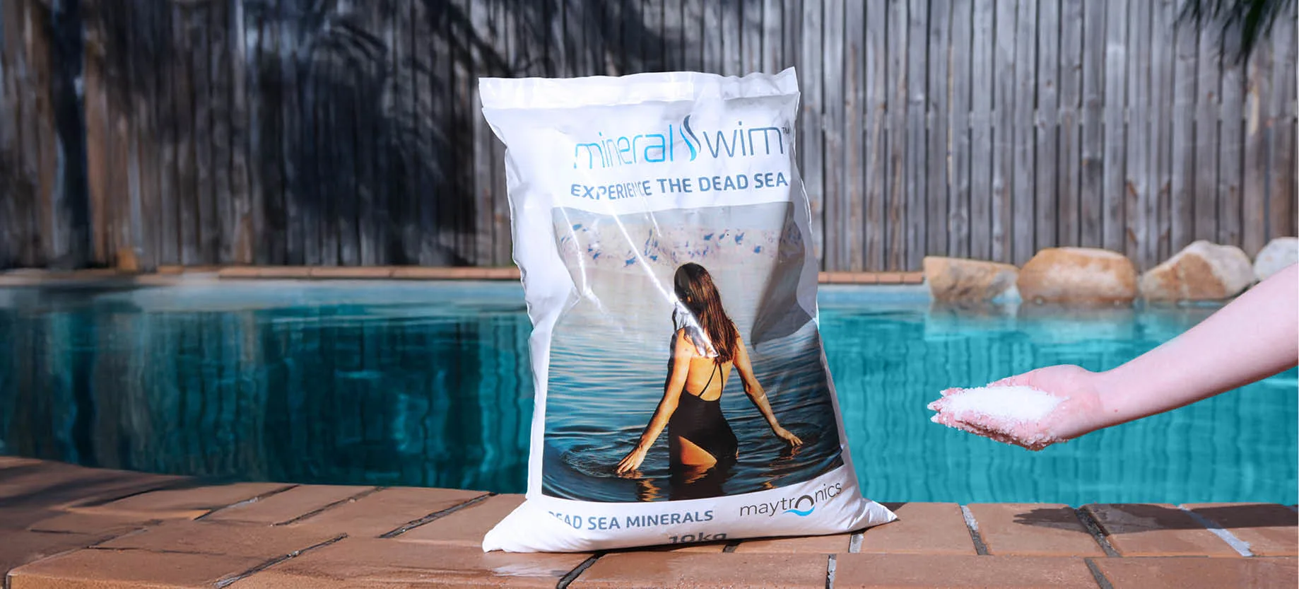Mineral Swim bag on a pool with a hand that has Mineral Swim chemicals.