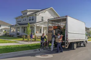 A family unloading a moving truck with a house in the background