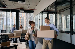 Two people talking in a corporate office while one person is holding boxes
