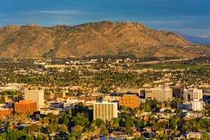 Aerial view of Riverside, CA with buildings in the foreground and mountains in the background.