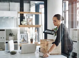A woman packing belongings in a box on a desk in an office.