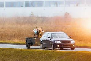 A car on the road with a tow trailer behind it carrying a motorcycle