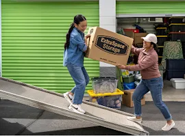 Mother and daughter carrying box from moving truck to storage unit