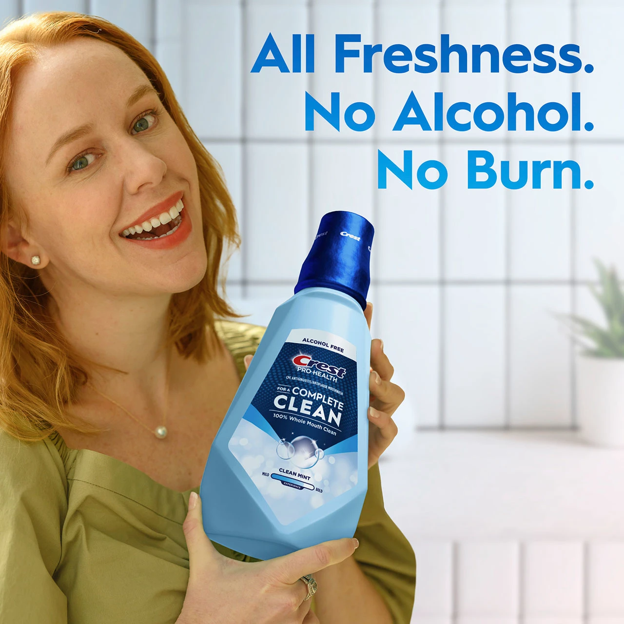 Smiling woman holding a bottle of Crest Pro‑Health Clean Mint mouthwash with text ‘All Freshness. No Alcohol. No Burn.’