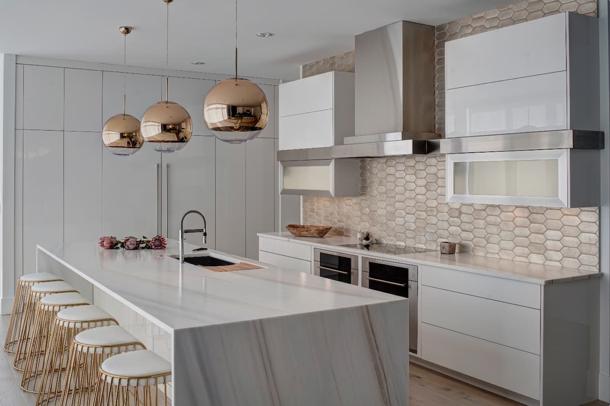 White kitchen with terracotta hand painted tiles, and glossy cabinetry, marble island and metallic fixtures