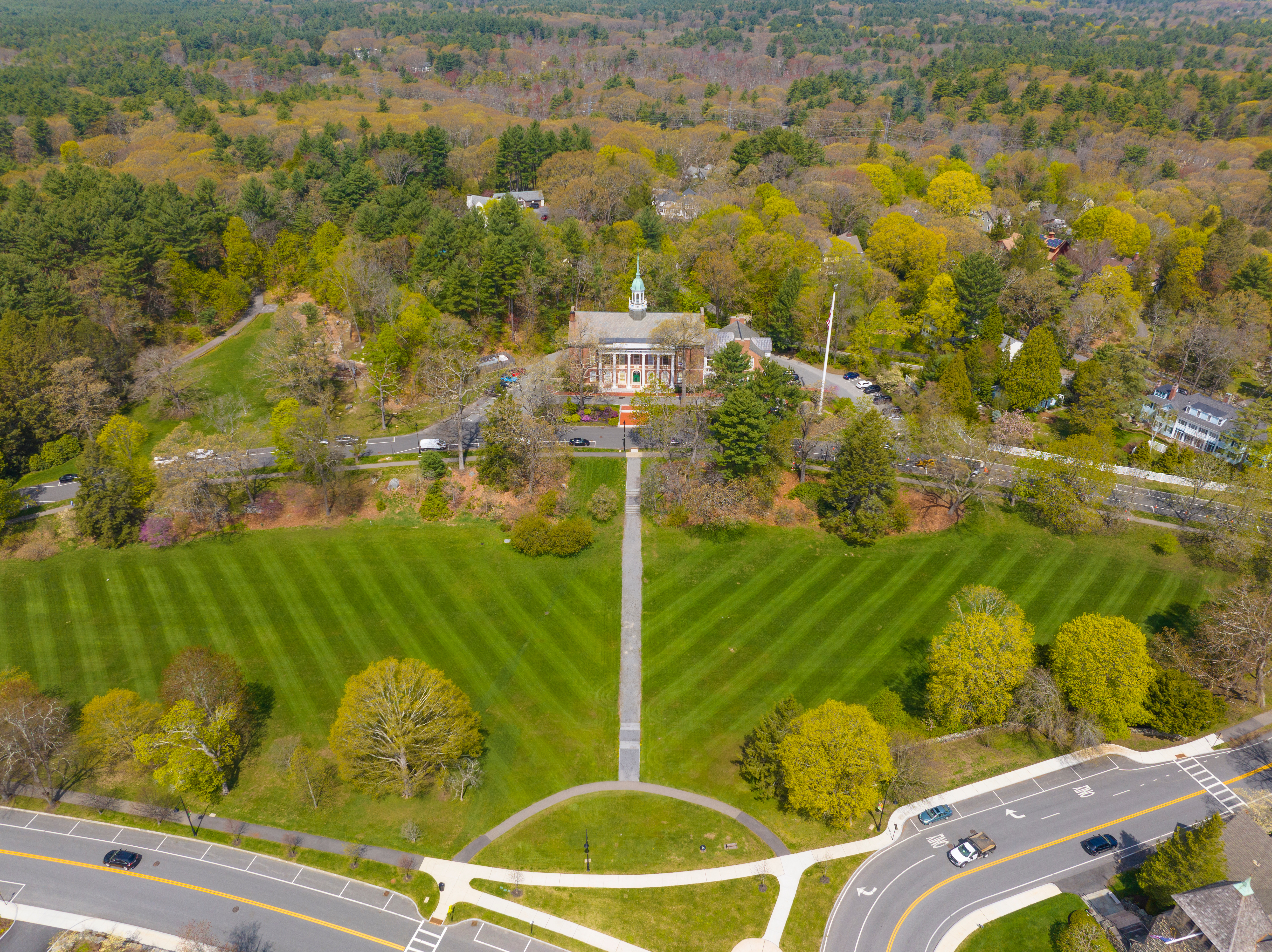 aerial view of a green park flanked by trees with large building with steeple in the background