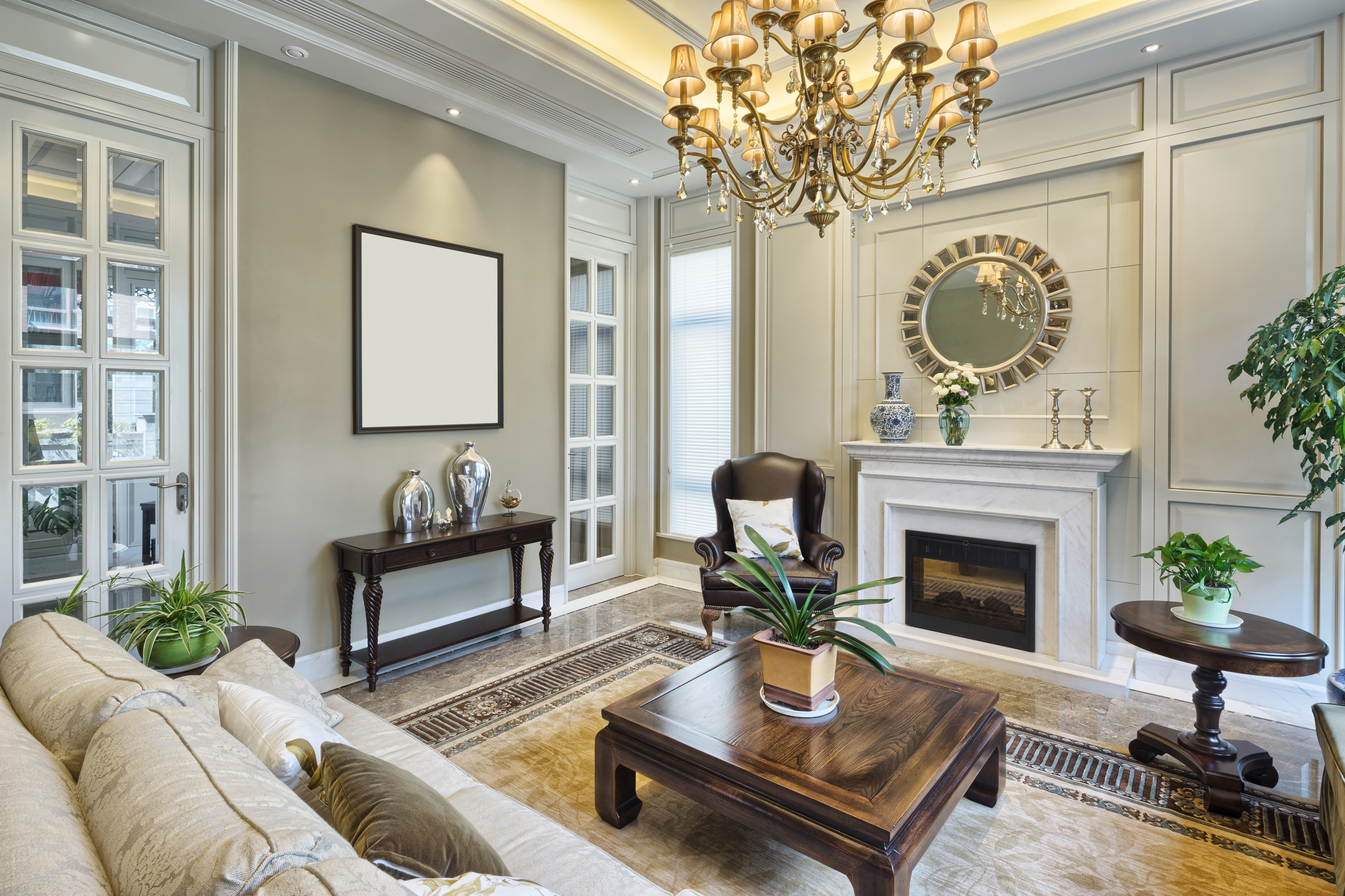Living room with white fireplace, wainscoting, ornate chandelier French doors and coffee table and sofa