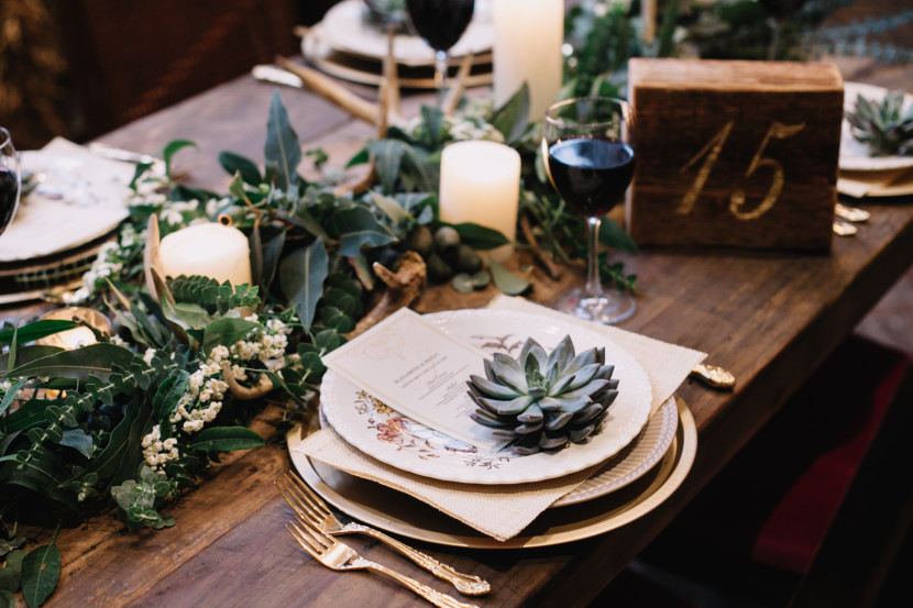 Wooden table with stacked place settings, garland, candles and succulents